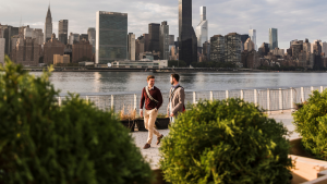 Two men walking along East River with NYC skyline in background