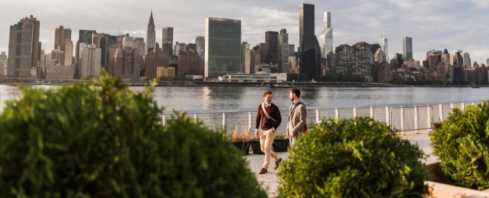 Two men walking along the East River with NYC skyline in background