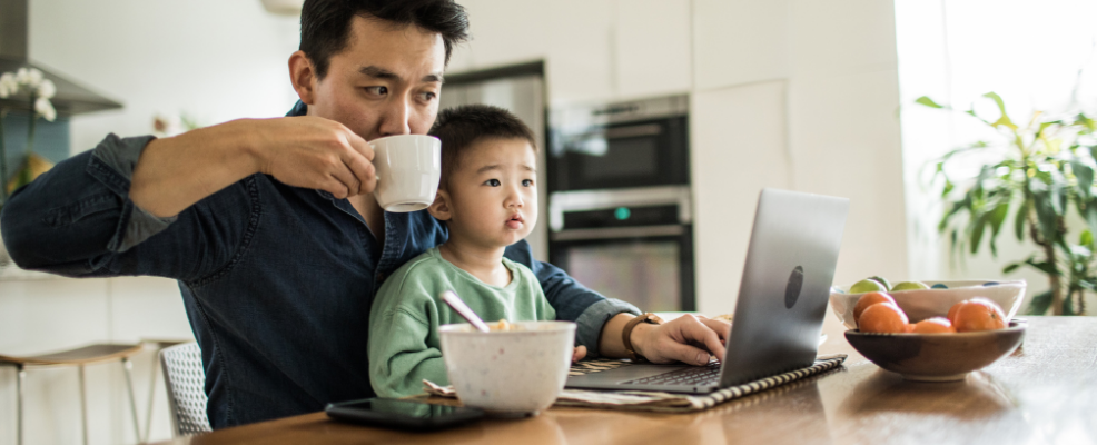 Father multi-tasking with young son at kitchen table